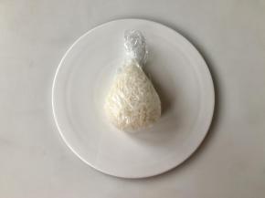 接着我们来做圣诞老人饭团。取110克左右的饭团，用保鲜膜包上，如图捏成水滴状。