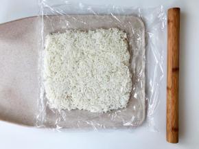 把米饭放在保鲜膜上，盖好，用擀面杖擀成一个方片。