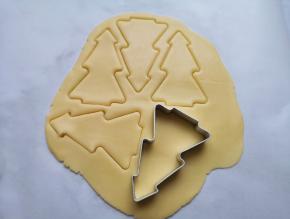 台面上铺一张油纸，先取一半原色面团放在油纸上擀开，用圣诞树模具压出圣诞树形状的饼干。