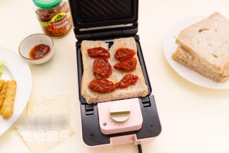 取出煎好的鸡排，在三明治机上先放一片吐司，吐司上放圣女果干，没有果干的可以涂一点番茄沙司。