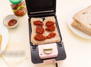 取出煎好的鸡排，在三明治机上先放一片吐司，吐司上放圣女果干，没有果干的可以涂一点番茄沙司。