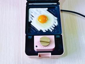 三明治机器连接电源，刷少许食用油，将一枚鸡蛋磕入，撒上1克盐。