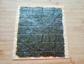 寿司帘上面铺上一张保鲜膜，放上一片寿司紫菜。