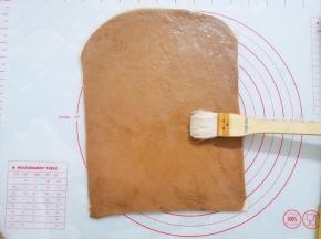 红色面团放在白色面团上面，将面片再次擀薄，刷上少许蜂蜜水