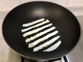 锅里再刷一层油，把蛋清层出切成条，如图每条间隔一样的宽度的放入锅中。