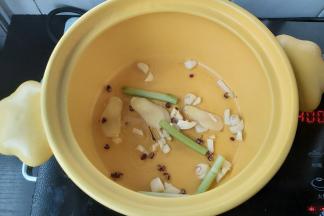 在砂锅内，淋一点点花生油，加入花椒、姜片、葱段、蒜末，轻轻炒香。