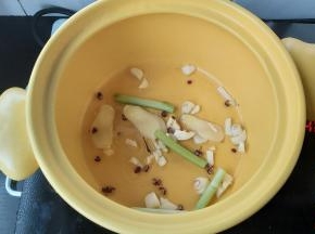 在砂锅内，淋一点点花生油，加入花椒、姜片、葱段、蒜末，轻轻炒香。