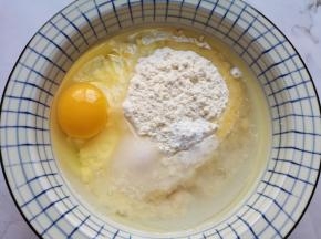 面粉中打入一个鸡蛋，加入盐、玉米油、泡打粉和温水。