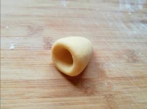 将圆锥形的面团放在左手手心里，用右手的大拇指放在圆锥形底部的中间位置，转圈旋出窝头的窝。