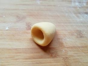 将圆锥形的面团放在左手手心里，用右手的大拇指放在圆锥形底部的中间位置，转圈旋出窝头的窝。