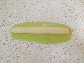 白色的长条状面团放在绿色的长方形面团上，卷起来。