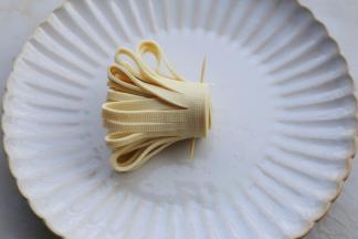 从一边顺着对折齐边的地方卷起，卷好的根部用牙签固定，立起就是一朵菊花了。