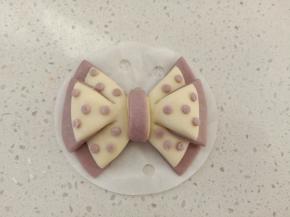 左边的整形同右边一样，中间的那条面团向上翻过去再压到下面，用之前剩余的紫色面团搓一些小圆球粘到蝴蝶结上面做点缀