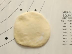 取一个面团用手掌按扁，边缘有气泡用手拍破即可。