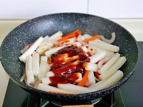 再加入年糕，调好的酱料汁，加入纯净水，水量没过年糕的半指即可，大火烧开，转小火煮至汤汁浓稠，一边煮一边用铲子翻炒。