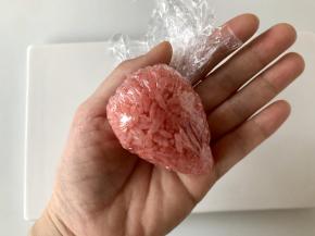 借助保鲜膜把米饭裹住馅料，然后捏成草莓的形状。