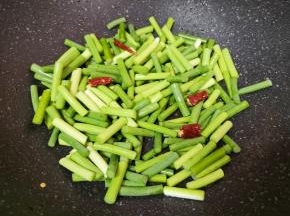 锅底留余油，下入蒜苔和干红辣椒，翻炒至变色。