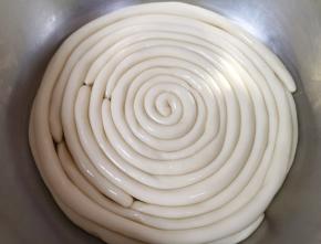 将一个个长条用手搓成手指粗细的圆棍形面条，抹上油盘在盆里，盖上保鲜膜饧3个小时以上。