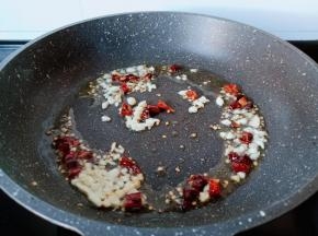 锅里冷油下蒜末与干辣椒段炒香。