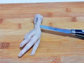 泡好的鸡爪去骨，首先将根部用水果刀划断开，再鸡爪背上划一刀，如图。