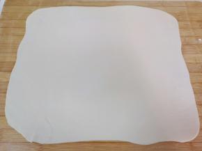 先取一半面团（另一半面团继续用保鲜膜盖上），擀成一张接近长方形的大面片。