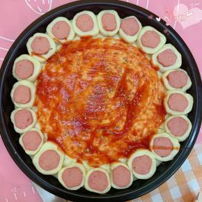 醒好的披萨饼皮边缘刷上清水易粘连，把香肠段摆上去。涂一层番茄酱，撒一些披萨草。