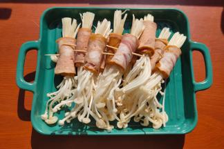 取一块培根把金针菇卷起来，用牙签固定，每份金针菇13-15g。