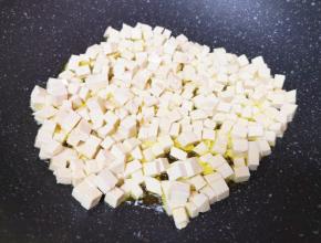老豆腐切成小丁，炒锅内倒适量的食用油烧热，下入豆腐丁中火翻炒。