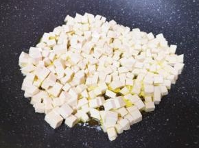 老豆腐切成小丁，炒锅内倒适量的食用油烧热，下入豆腐丁中火翻炒。