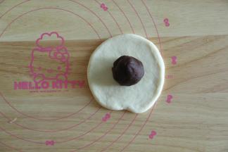 取一个松弛好的面团，擀开，翻面，放上一个馅料球。然后将面皮贴合在馅料球上，用右手虎口慢慢将面团收口，我习惯这样收口，比较均匀。收口一定要收紧，不然烤的时候容易漏馅料。