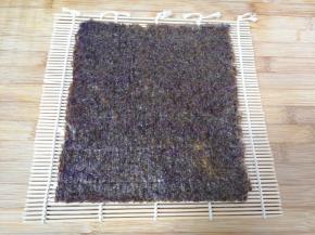 寿司帘上面铺上一张保鲜膜，放上一片寿司紫菜。