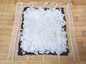 用勺子将米饭均匀的铺在紫菜上面压实。