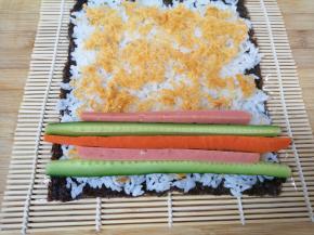 依次摆上黄瓜、火腿肠和胡萝卜条，从一头卷起，卷好以后用劲捏紧。