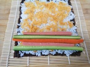 依次摆上黄瓜、火腿肠和胡萝卜条，从一头卷起，卷好以后用劲捏紧。
