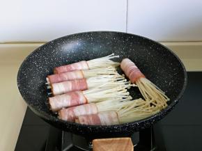 平底锅中刷上食用油，摆入培根金针菇卷。(固定好后可以将牙签取下来，培根收口朝下煎)