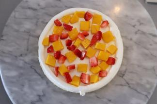 将一片蛋糕片放在裱花台上，表面抹上打发好的淡奶油，放上水果粒，再用淡奶油抹平。