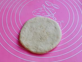 取一块面团，用擀面杖擀圆饼，撒上白芝麻，再来回擀，将芝麻压实。