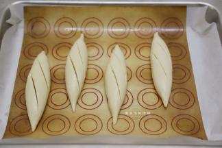 戴着手套抓起面团放入碱水，两面浸泡各20秒左右，捞出沥干水分放入垫有油布的烤盘里，用割包刀快速割出两道口子，要深，快，准，拖拖拉拉的切割，最后的裂口都不会好看哦。