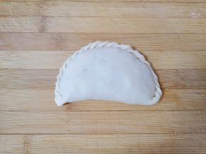 捏花边，先提起一角向内折，然后继续拉起卷过去，一直到捏完，最后的小角直接折回来压紧，一个花边韭菜盒子就做好了。