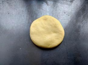 面团醒好后，根据烤箱的大小分小剂子，我的烤箱是62升的烤盘比较大，每个小剂子约80-85g，取出一块面团，用手压扁，不需要擀面杖，面团是非常软的，直接放在手掌上压扁即可。（面团一次不能全部烘烤，每次分出适合的小剂子，余下的保鲜膜密封保存）