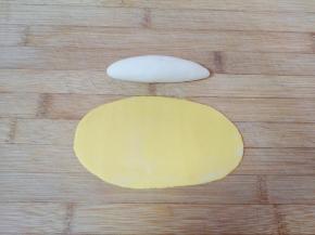 白色的小剂子搓成长条状，黄色的小剂子擀成椭圆形的面皮（黄色面皮的大小一定要能包的住白色的长条状面团），如图。