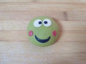 分别用其它颜色的面团做好小青蛙的眼睛、红脸蛋和嘴巴，沾水贴在绿色的豆沙包上面，一个小青蛙豆沙包就做好了，依次做完剩下的小青蛙豆沙包，造型可根据自己的喜好随意发挥。