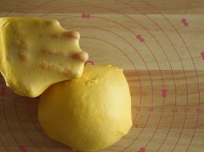 先转1或2档，将黄油和面团打到融合，再转3-4档打到扩展。面团光滑挂在打面钩上，能扯出透明结实的膜。取下面团，双手握住面团，朝外侧折叠收圆面团。特地切了一小块，轻轻扯开给你们看下膜。面包不需要像吐司一样打到完全的手套膜。