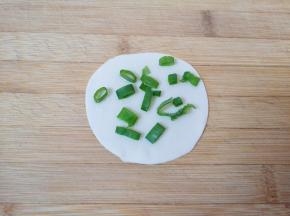 取一张饺子皮稍微擀大一点，刷上一层熟油，撒上盐，放上香葱叶。