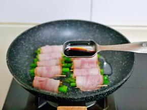 平底锅中刷少许食用油，摆放上芦笋培根卷，再加入1小勺生抽。