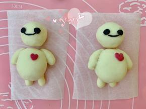 取2g白面团，加入少许竹炭粉和几滴牛奶揉成黑色面团。取绿豆大小的黑色面团揉成小圆球，再用手指轻轻压扁，作为眼睛。取一点黑色面团搓成细线，作为嘴巴。沾水粘在头上即可。