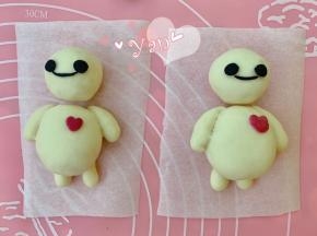 取2g白面团，加入少许竹炭粉和几滴牛奶揉成黑色面团。取绿豆大小的黑色面团揉成小圆球，再用手指轻轻压扁，作为眼睛。取一点黑色面团搓成细线，作为嘴巴。沾水粘在头上即可。