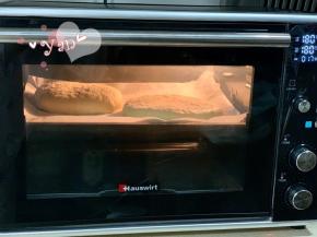 盖上保鲜膜发酵半小时，发至体积比原来略厚的状态即可。用牙签在表面戳一些小洞，以便烘烤膨胀时排出饼内多余的空气。撒上卡夫芝士粉，再筛入适量玉米面粉。放入烤箱中层，180度烤18分钟。烘烤过程中为避免上色过深，请及时加盖锡纸。