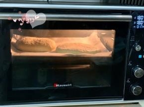 盖上保鲜膜发酵半小时，发至体积比原来略厚的状态即可。用牙签在表面戳一些小洞，以便烘烤膨胀时排出饼内多余的空气。撒上卡夫芝士粉，再筛入适量玉米面粉。放入烤箱中层，180度烤18分钟。烘烤过程中为避免上色过深，请及时加盖锡纸。