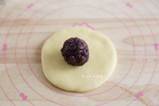 将面团擀成中间厚一些的圆形，包入蜜豆馅。